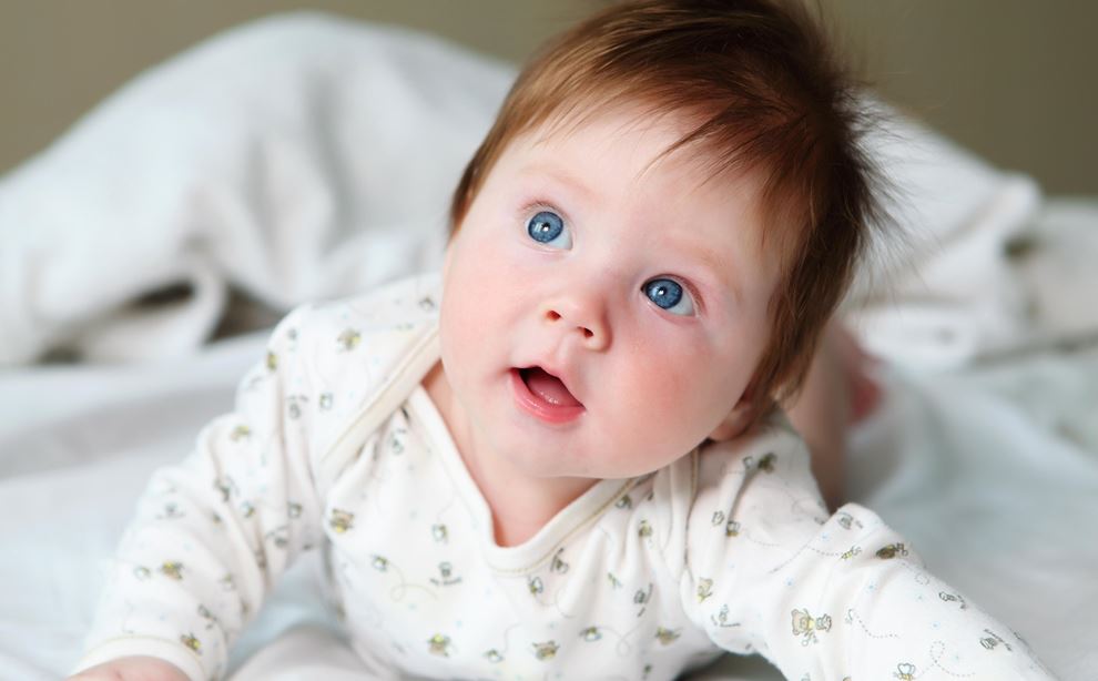Mørkhåret baby med blå øjne, der ligger på maven